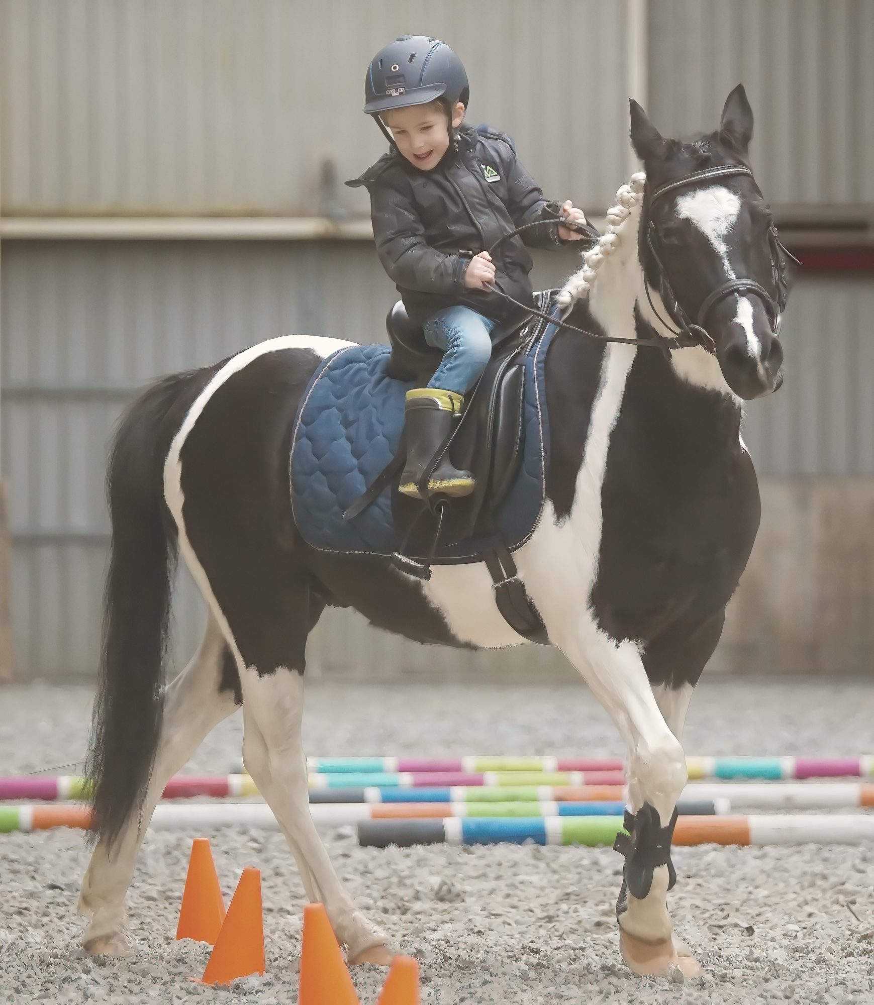 Een lachend kind op een bonte pony tijdens een ponyles