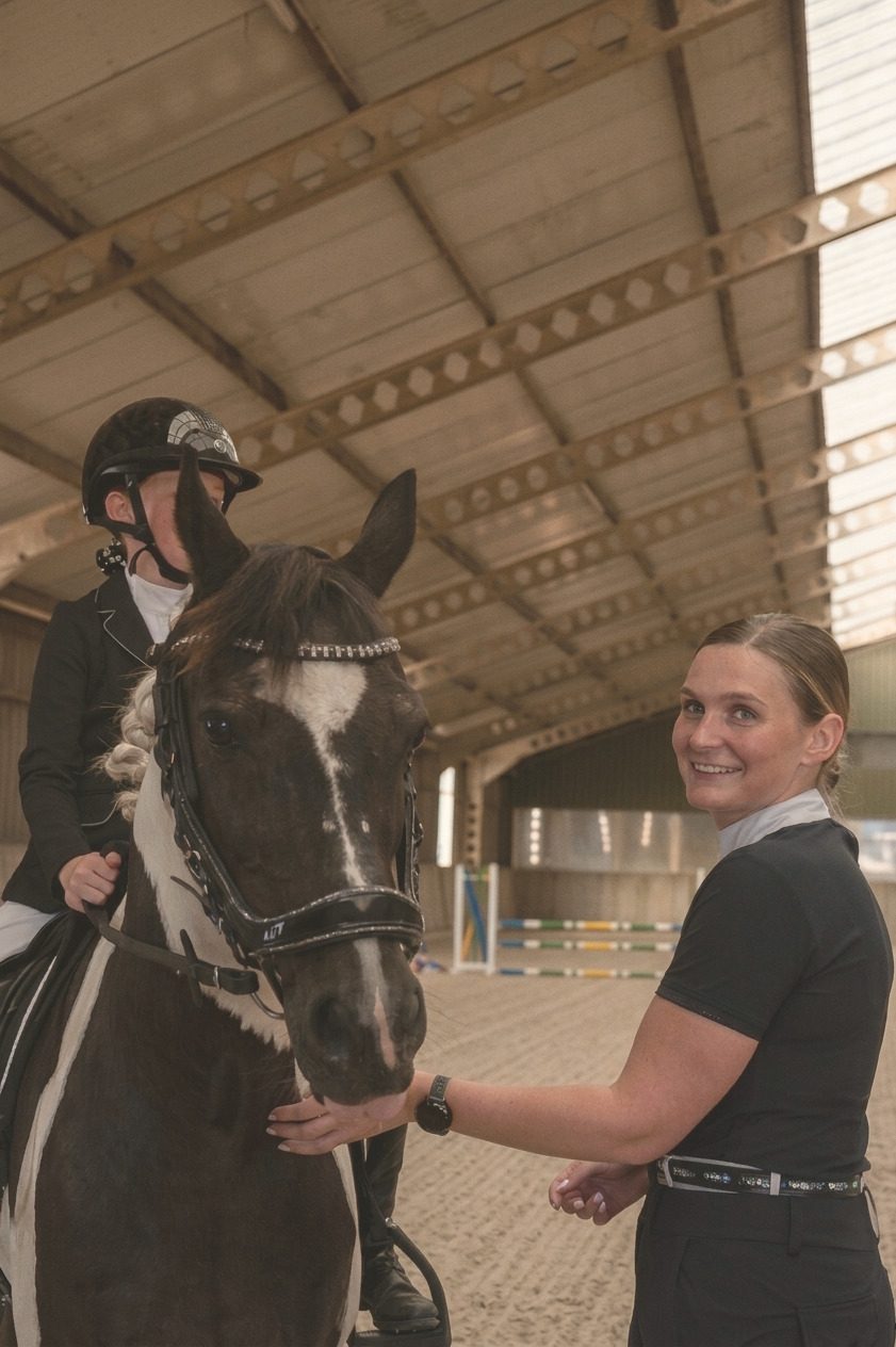 Lisa naast een pony met een jonge ruiter erop